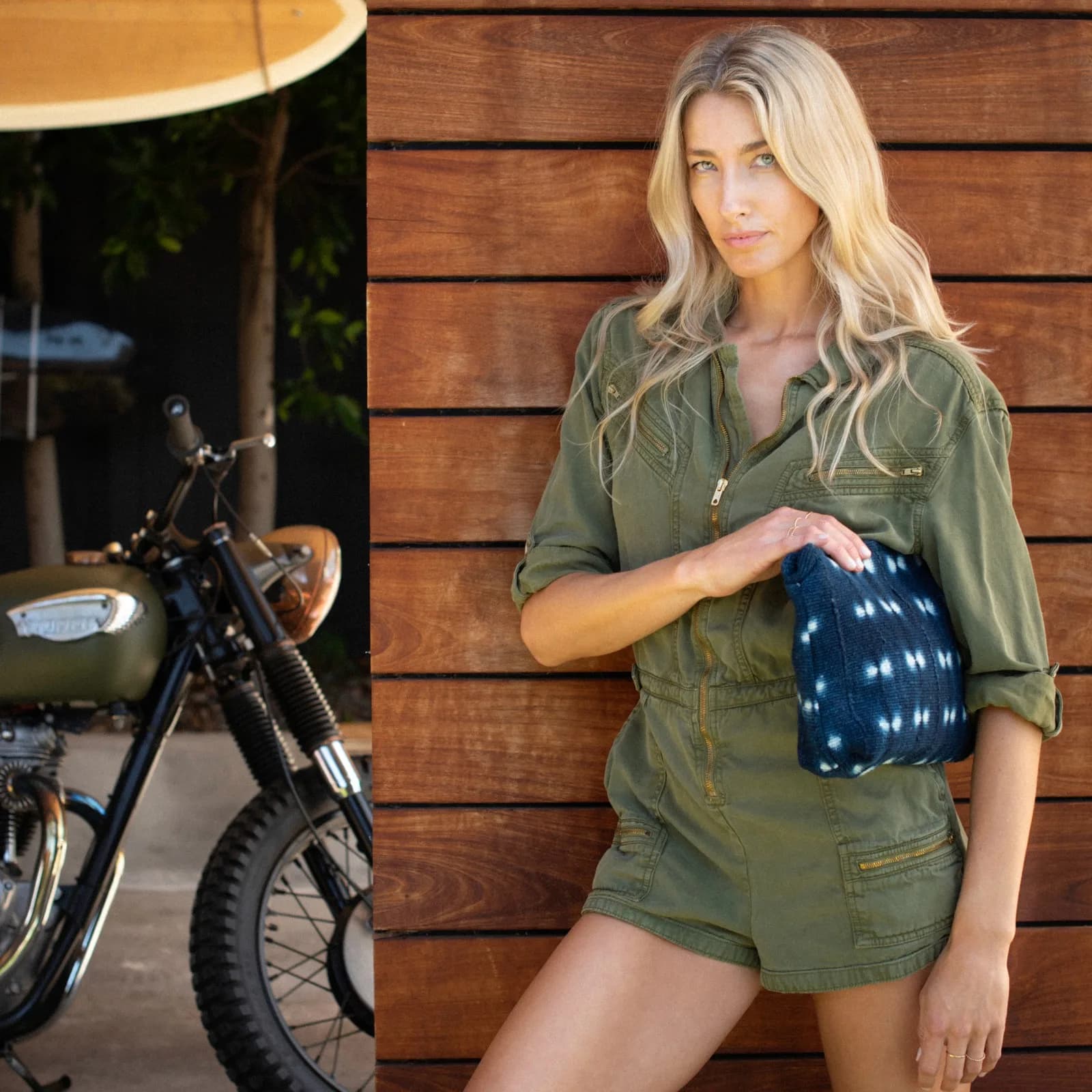 Model in olive utility set beside a vintage motorcycle